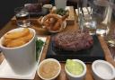 Main: Ribeye steak 280g served with thick cut chips, rocket salad, sea salt, garlic butter, and peppercorn sauce, with a side of onion rings. Picture: Louisa Baldwin