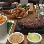 Main: Ribeye steak 280g served with thick cut chips, rocket salad, sea salt, garlic butter, and peppercorn sauce, with a side of onion rings. Picture: Louisa Baldwin